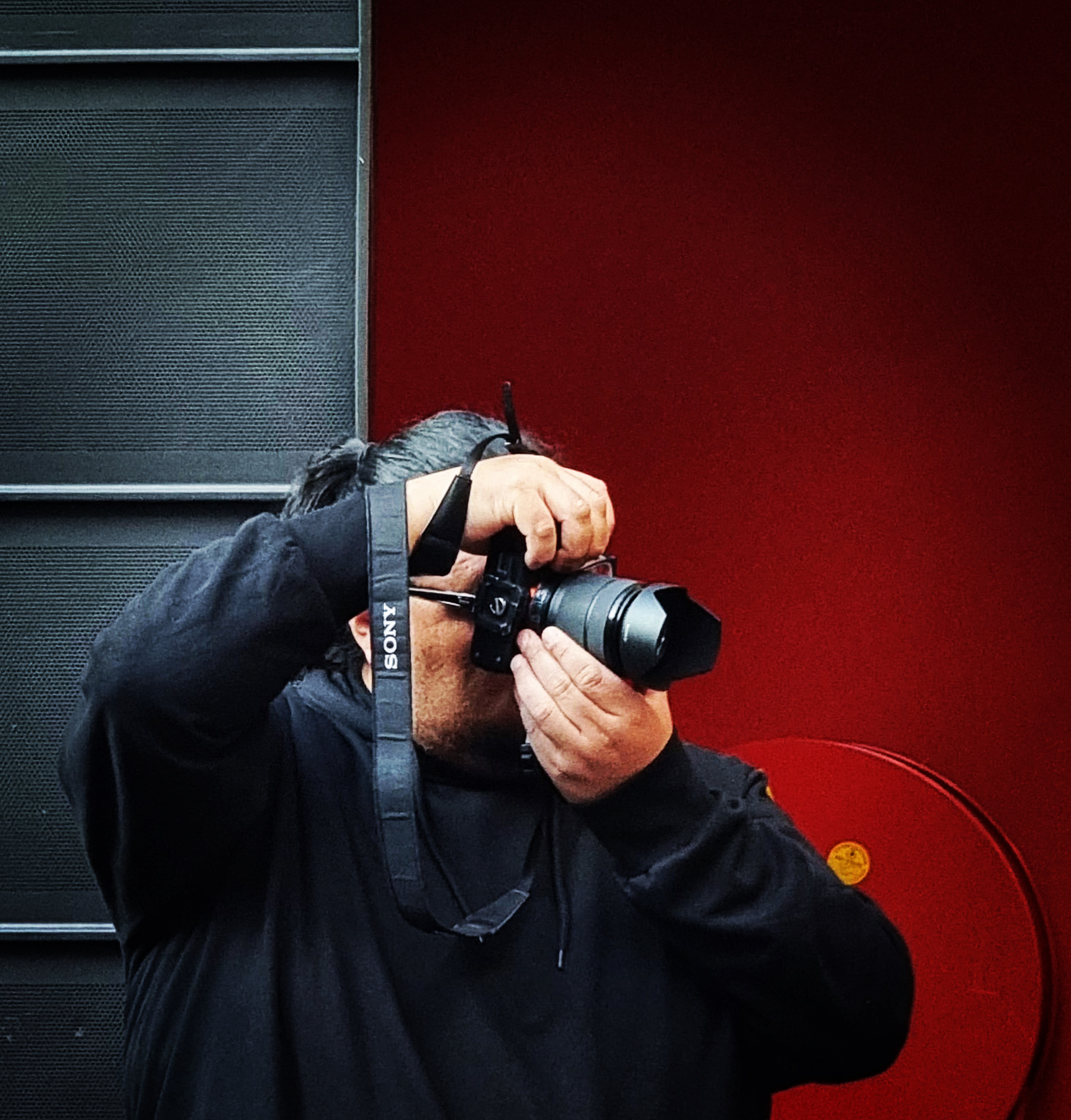 Fotograaf aan het werk met een camera voor een rode wand.